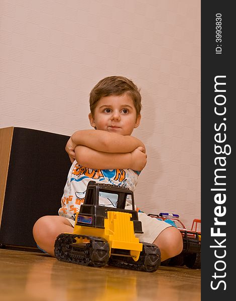 The little boy sitting on a floor with toys.