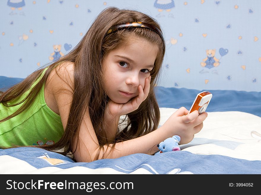 The girl lays on a bed and holds phone.