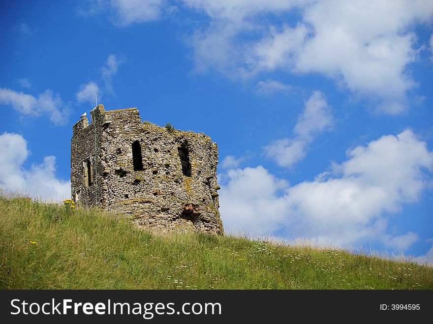 The remains of a medieval tower with green grass in the foreground and a blue sky in the background. The remains of a medieval tower with green grass in the foreground and a blue sky in the background.