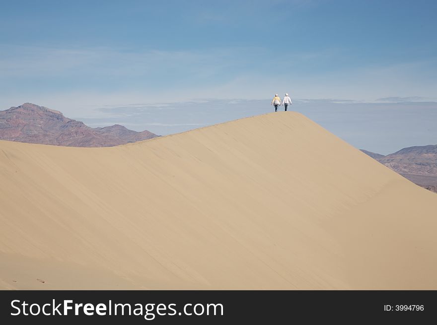 A couple walking along the crest of a dune in Death Valley, CA. A couple walking along the crest of a dune in Death Valley, CA