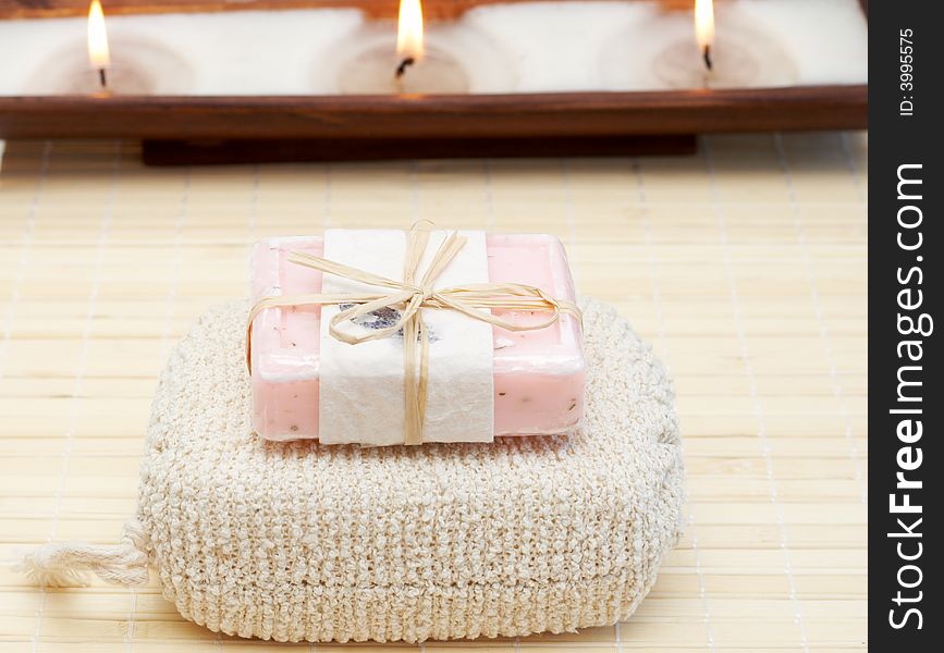 Relaxing spa scene with body products - exfoliating sponge and handmade soap with candles in the background