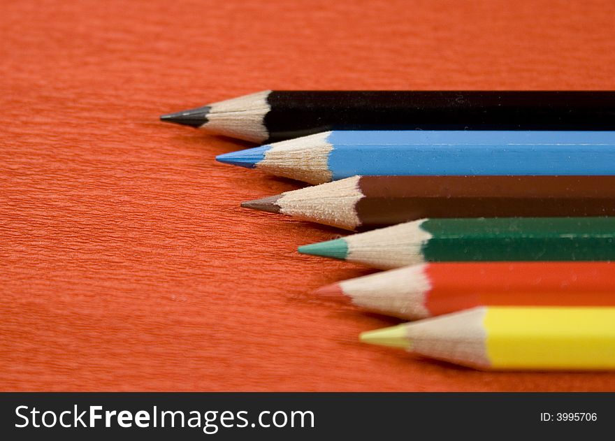 Six colored pencils over red background