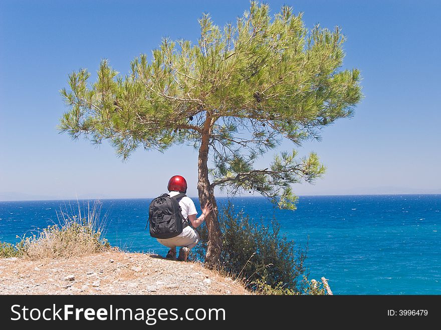 Hiker by a pine-tree on a steep above the sea. Samos island, Greece. Hiker by a pine-tree on a steep above the sea. Samos island, Greece.