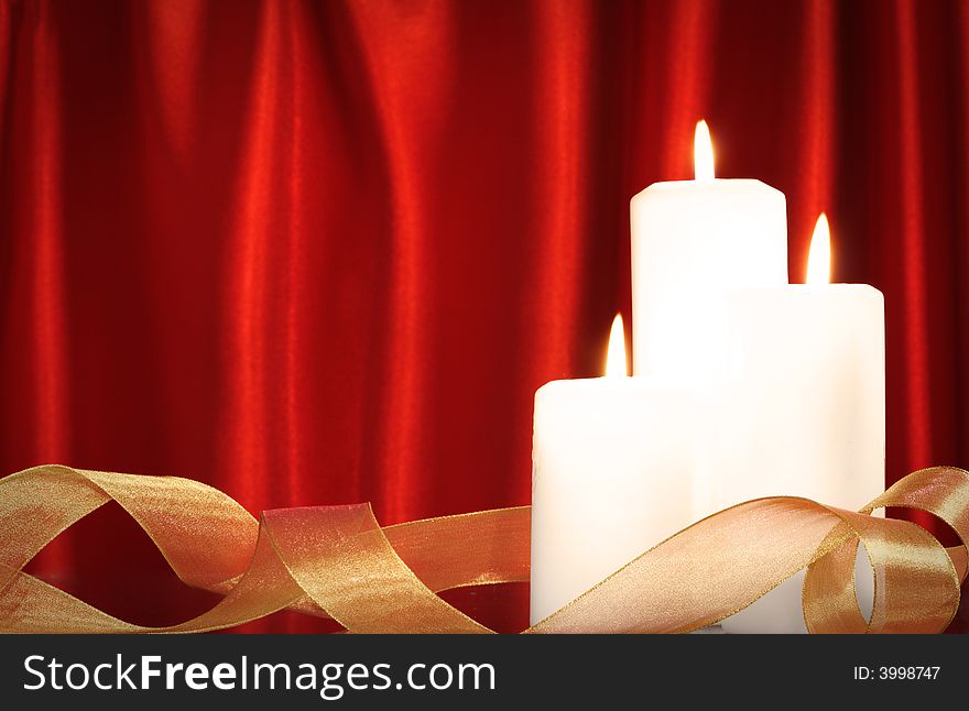 Candles and golden ribbon in front of red satin background. Candles and golden ribbon in front of red satin background