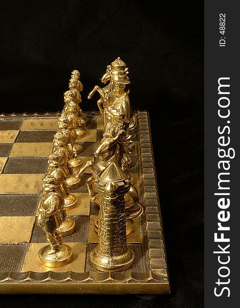 Closeup of an unique chess board with brass (white) side lineup. Very deep DOF so that all the pieces are in focus. Black background. Closeup of an unique chess board with brass (white) side lineup. Very deep DOF so that all the pieces are in focus. Black background.