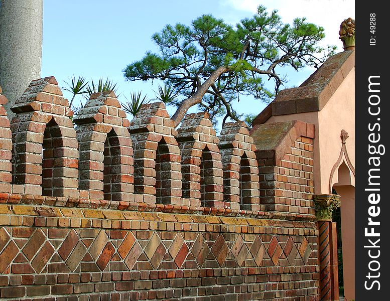 Multi-colored brick wall with decorative arches on top, with background of pine tree and blue sky. Multi-colored brick wall with decorative arches on top, with background of pine tree and blue sky