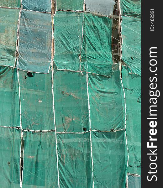 A building being constructed with scaffolding and protective netting all around, side view showing the layered colour and texture of the building, scafolding, and protective netting. A building being constructed with scaffolding and protective netting all around, side view showing the layered colour and texture of the building, scafolding, and protective netting.