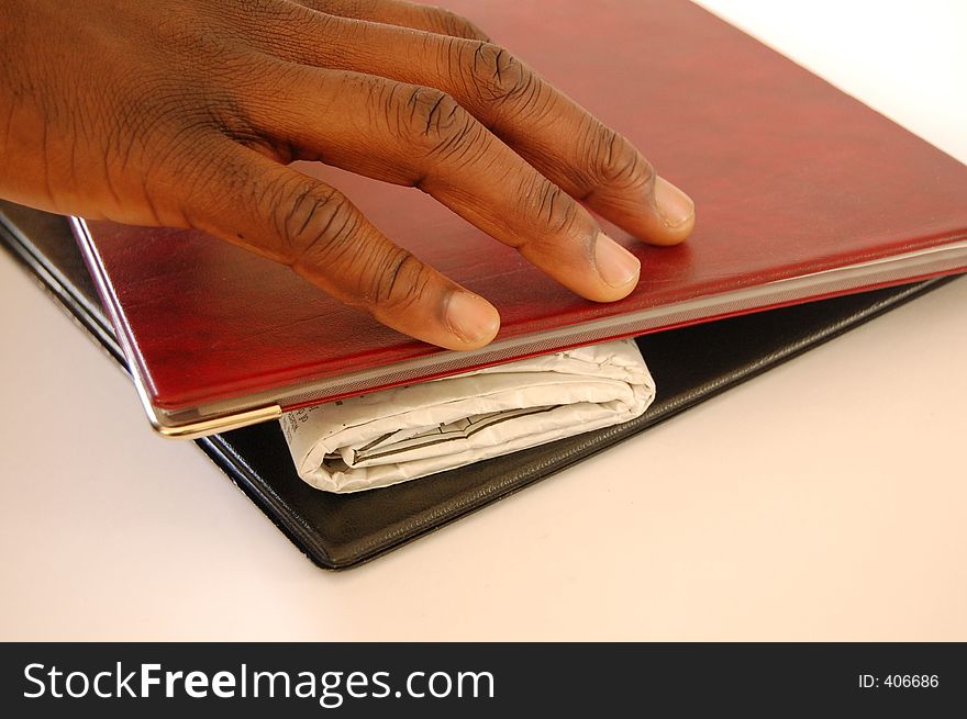 This is an image of a black hand reaching for a rolled up newspaper in between a set of portfolios. This is an image of a black hand reaching for a rolled up newspaper in between a set of portfolios.