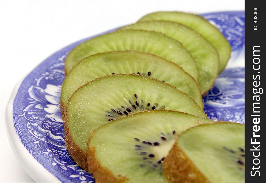 Row of kiwi slices on a plate.The focus is on the 2-3 rd pieces.