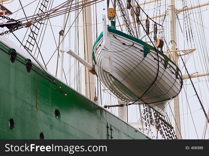 A small rescue boat hanging beside a large clipper ship. A small rescue boat hanging beside a large clipper ship.