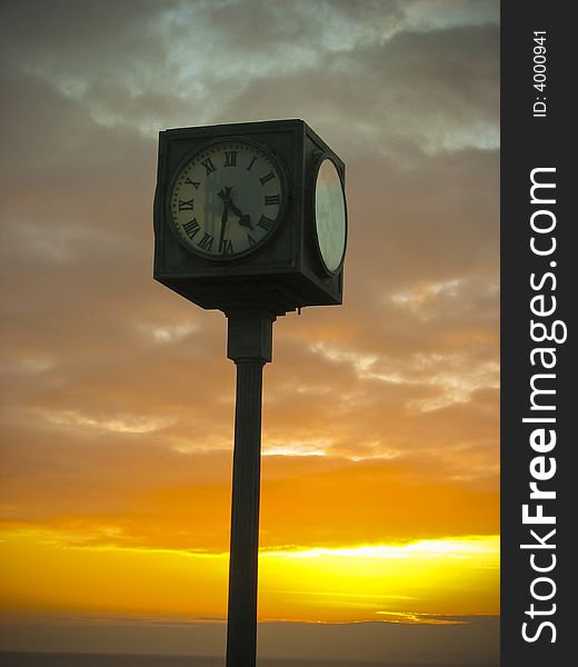A clock in the foreground and sunset in the background