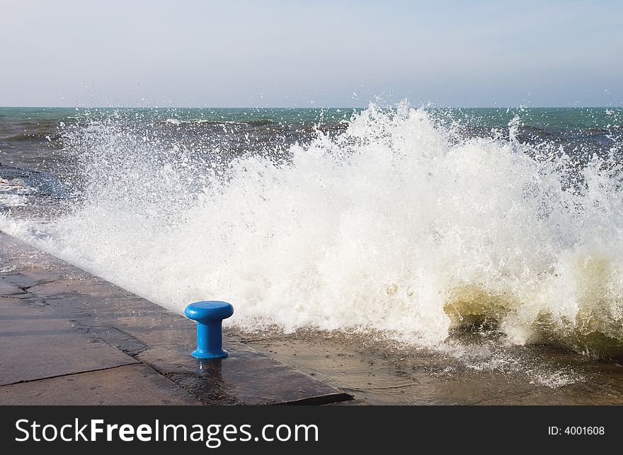 Lake Michigan wave crashing into the pier, with blue mooring bollard, at the channel mouth in Grand Haven. Lake Michigan wave crashing into the pier, with blue mooring bollard, at the channel mouth in Grand Haven