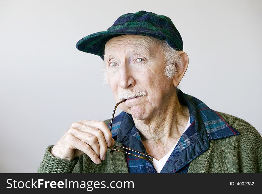Portrait of a thoughtful senior citizen with glasses wearing a hat. Portrait of a thoughtful senior citizen with glasses wearing a hat.