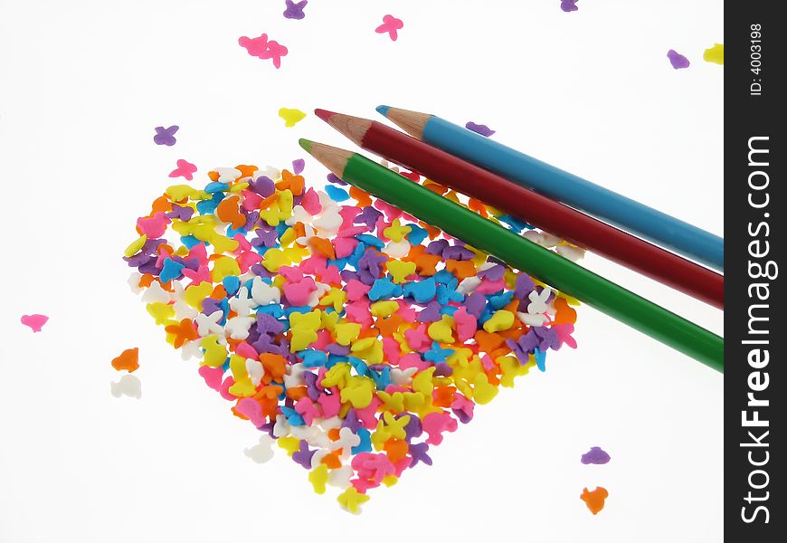 Crayons together with colorful candies shaped in heart form placed on white background. Crayons together with colorful candies shaped in heart form placed on white background