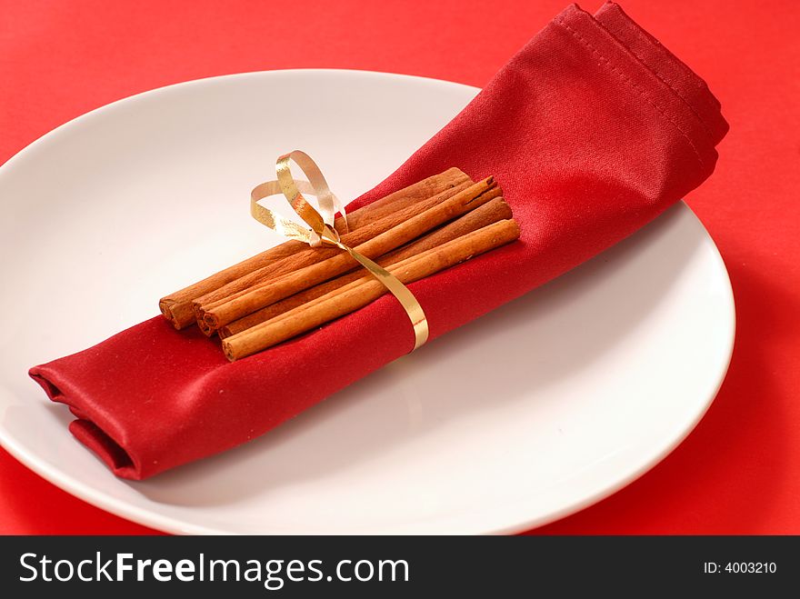 Several cinnamon sticks wrapped around a red napkin with a gold ribbon. Several cinnamon sticks wrapped around a red napkin with a gold ribbon