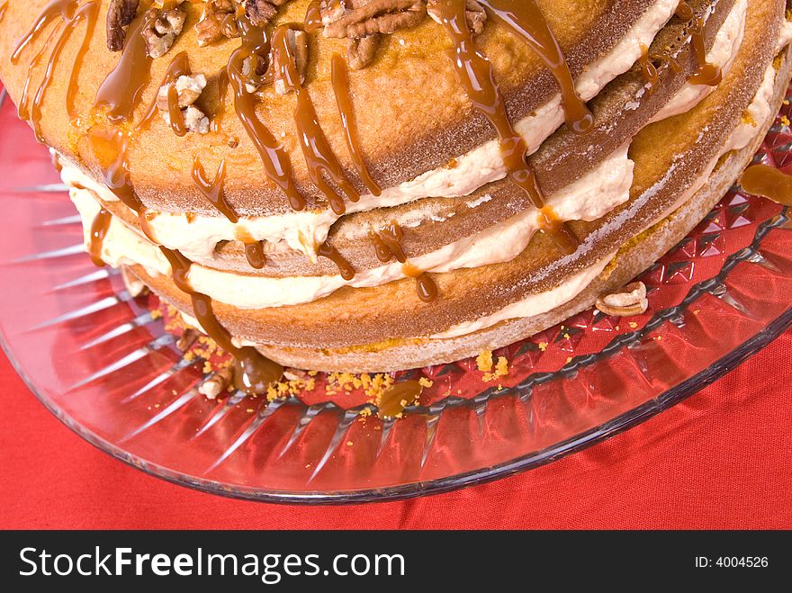 Sweet pumpkin cake dessert with cream filling and pecans on top drizzled with caramel topping on clear plate. Sweet pumpkin cake dessert with cream filling and pecans on top drizzled with caramel topping on clear plate