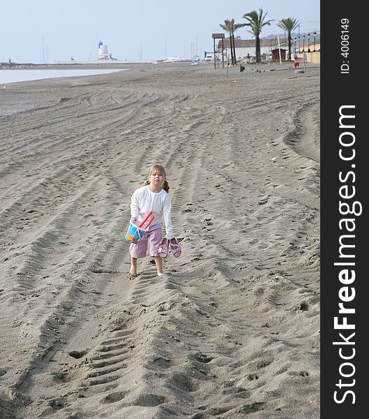 A young girl walking along the beach looking fed up carrying her bucket and spade. A young girl walking along the beach looking fed up carrying her bucket and spade