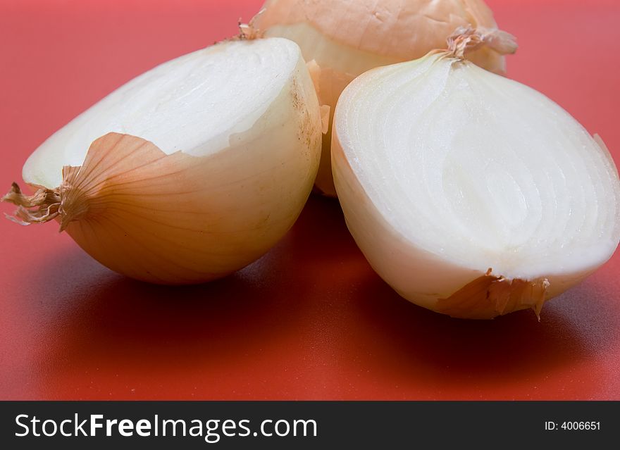 Two brown onions - one whole - one halved - on a red cuuting board