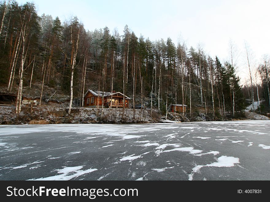 Wooden cottage in the forest and lake in winter