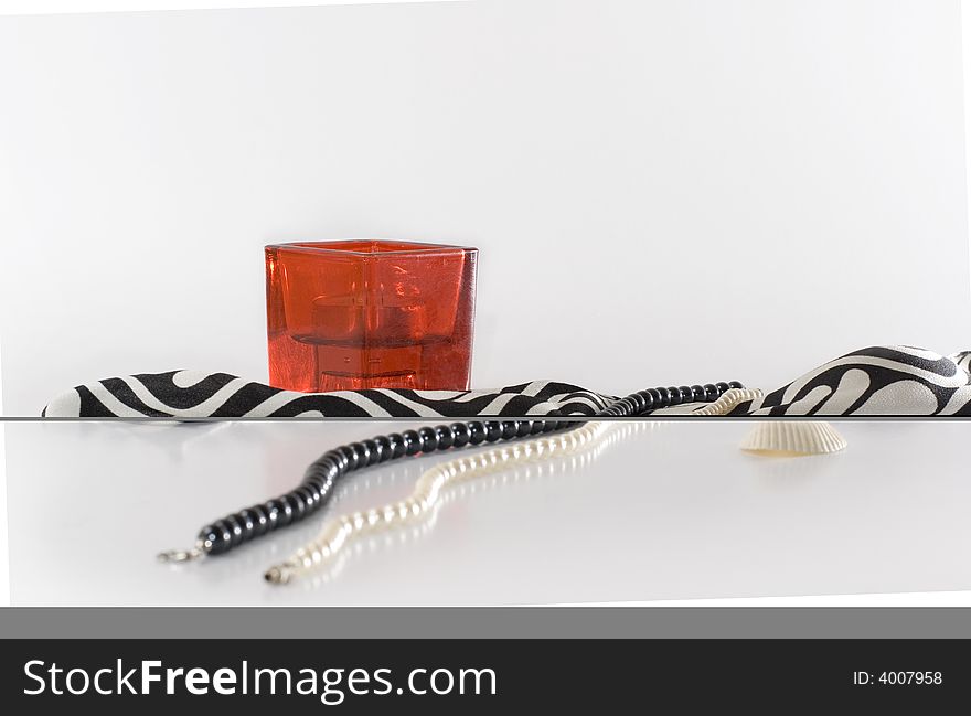 Strings of white and black  pearls with a scarf, a candle and a shell isolated on white background with dim reflexions. Strings of white and black  pearls with a scarf, a candle and a shell isolated on white background with dim reflexions