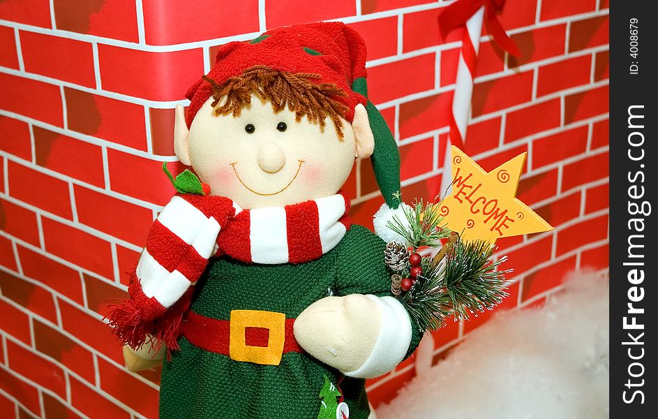 A colorfully stuffed toy snowman holding a welcome sign, all dressed up in winter clothing against a red brick background. A colorfully stuffed toy snowman holding a welcome sign, all dressed up in winter clothing against a red brick background.