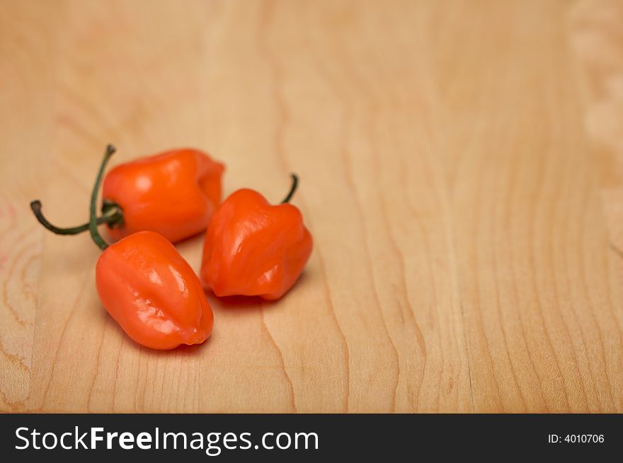 Three Orange Chili Peppers on a Wood Cutting Board. Room for Copy.