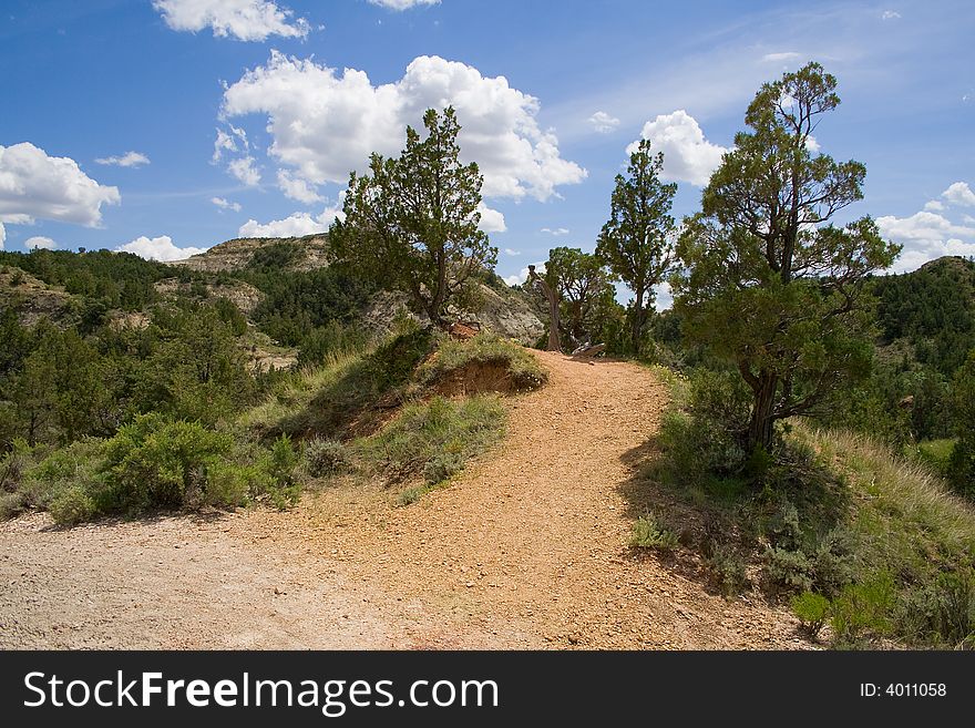 Scoria trail in the badlands with cedar trees, blue sky and clouds. Scoria trail in the badlands with cedar trees, blue sky and clouds