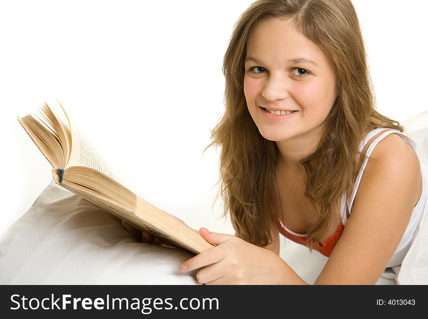 Young smiling girl reading book in bed.