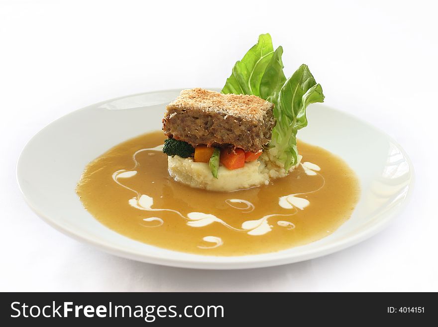 Gourmet meatloaf on a bed of vegetables and mash garnished with trimmed lettuce