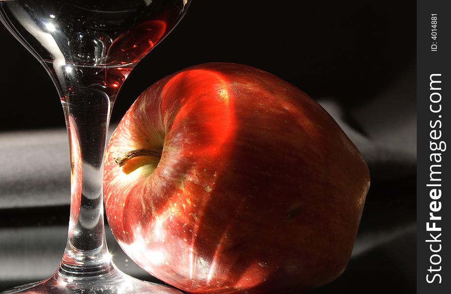 Wineglass and fresh red apple with lighting effects on dark gray