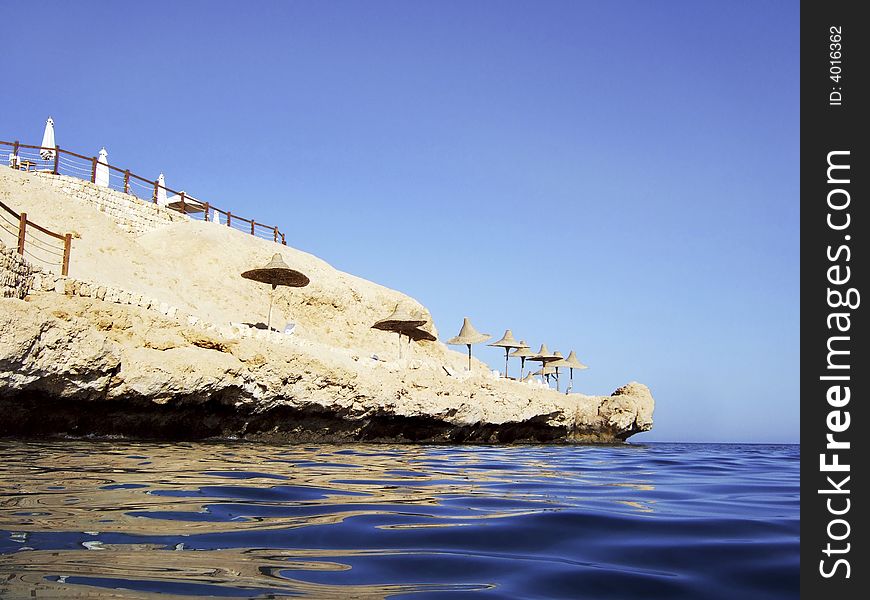 Small rocky beach with sun shades viewed from the sea. Small rocky beach with sun shades viewed from the sea