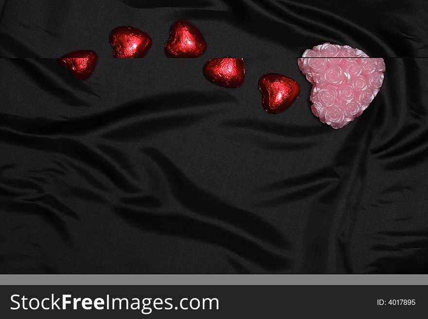 Heart shaped candies and candle on black satin with space for text. Heart shaped candies and candle on black satin with space for text