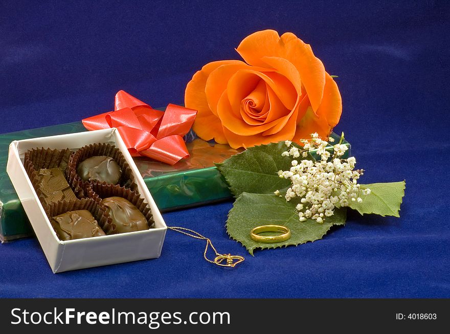 A closeup view of a chocolates on a box with a peach colored rose and gold necklace and baby's breath. A closeup view of a chocolates on a box with a peach colored rose and gold necklace and baby's breath.