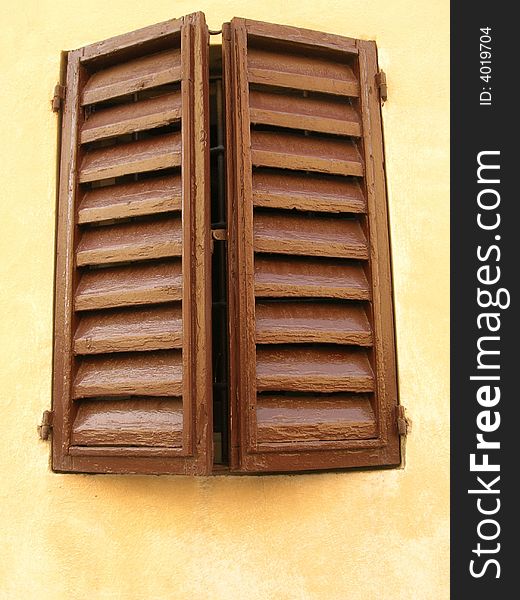 Two brown closed window shutters on a beige wall of a house in Italy