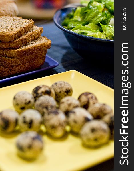 Table setting of a plate of quail eggs, slices of bread and green salad. The focus is on the background. Table setting of a plate of quail eggs, slices of bread and green salad. The focus is on the background.