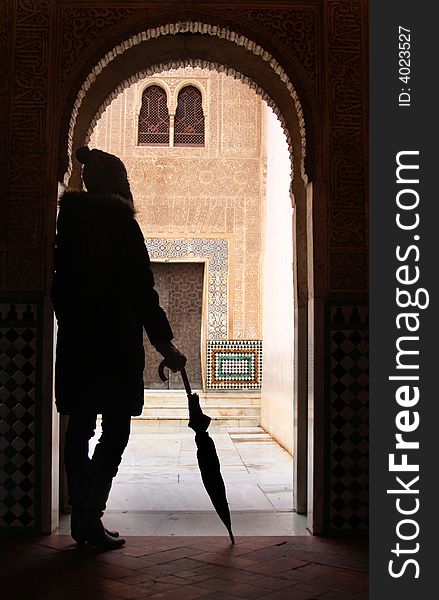 A modern woman looks through a doorway to an ancient royal courtyard at The Alhambra, Spain. A modern woman looks through a doorway to an ancient royal courtyard at The Alhambra, Spain.