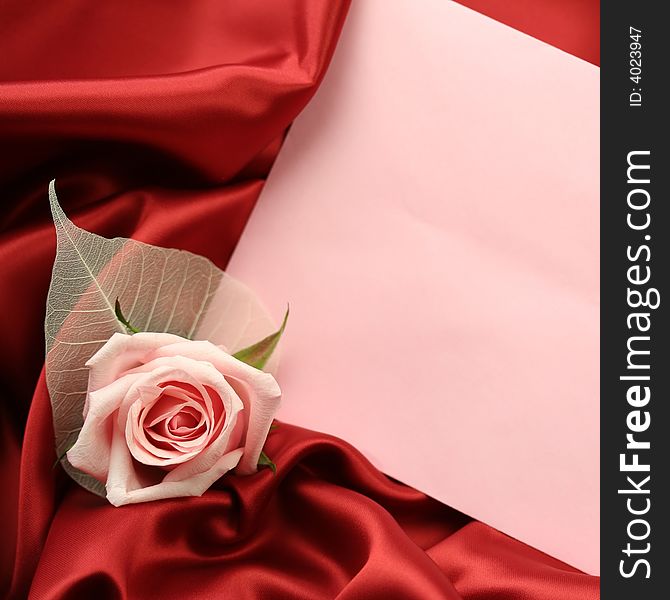 A detail of a pink rose with an empty pink card lying on dark red satin fabric. A detail of a pink rose with an empty pink card lying on dark red satin fabric.