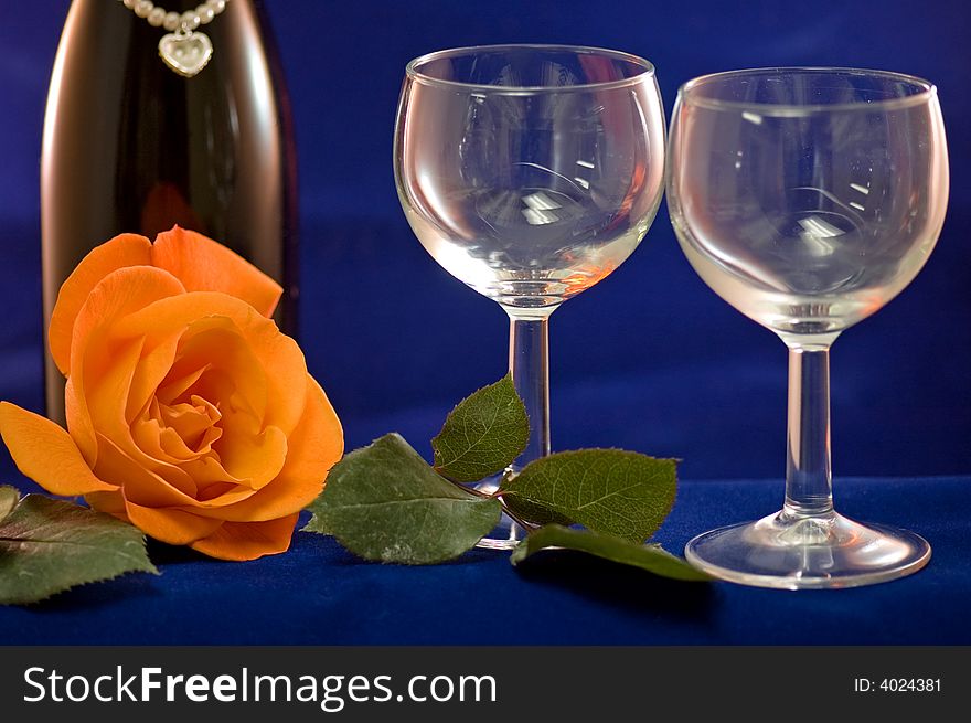 A closeup view of two empty wine glasses and a peach rose with a bottle of wine in the background. A closeup view of two empty wine glasses and a peach rose with a bottle of wine in the background.