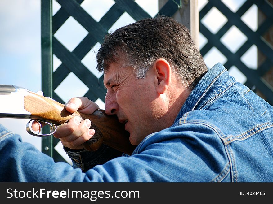Man in blue jeans jacket takes aim with rifle. Man in blue jeans jacket takes aim with rifle