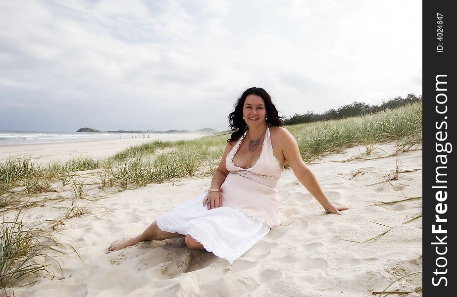 An attractive caucasian white woman sitting in the sand dunes on the beach. An attractive caucasian white woman sitting in the sand dunes on the beach