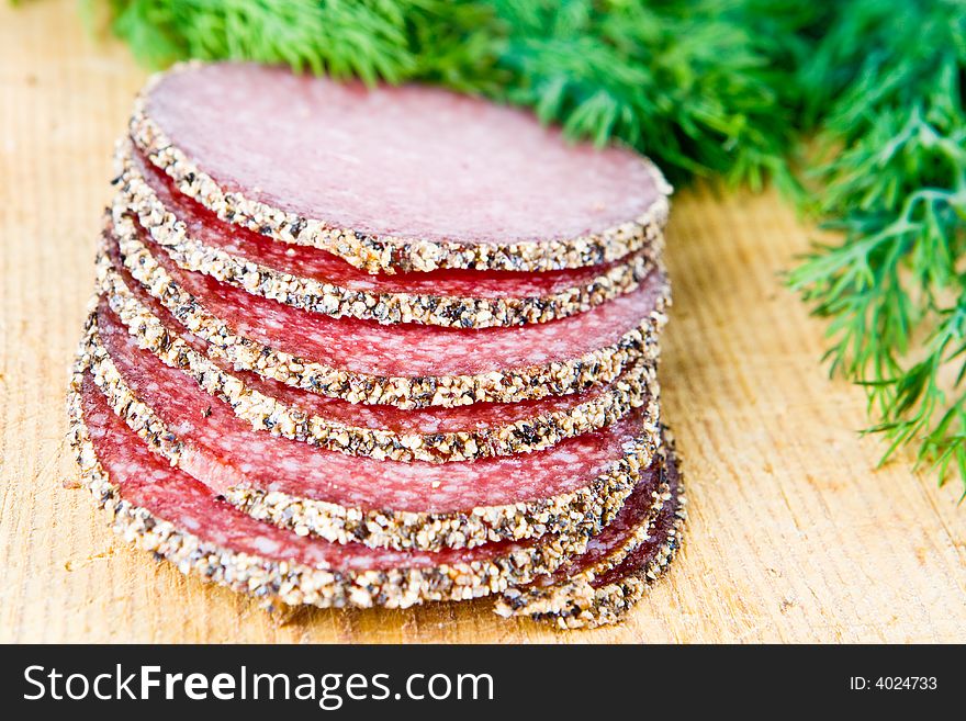 Peppered salami with dill on a wooden chopping block