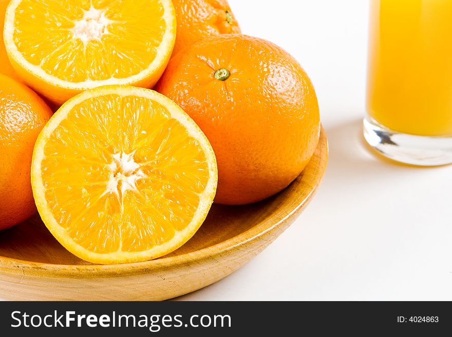 Two halves of orange in a wooden bowl with uncut oranges and a glass of orange juice in the background. Two halves of orange in a wooden bowl with uncut oranges and a glass of orange juice in the background