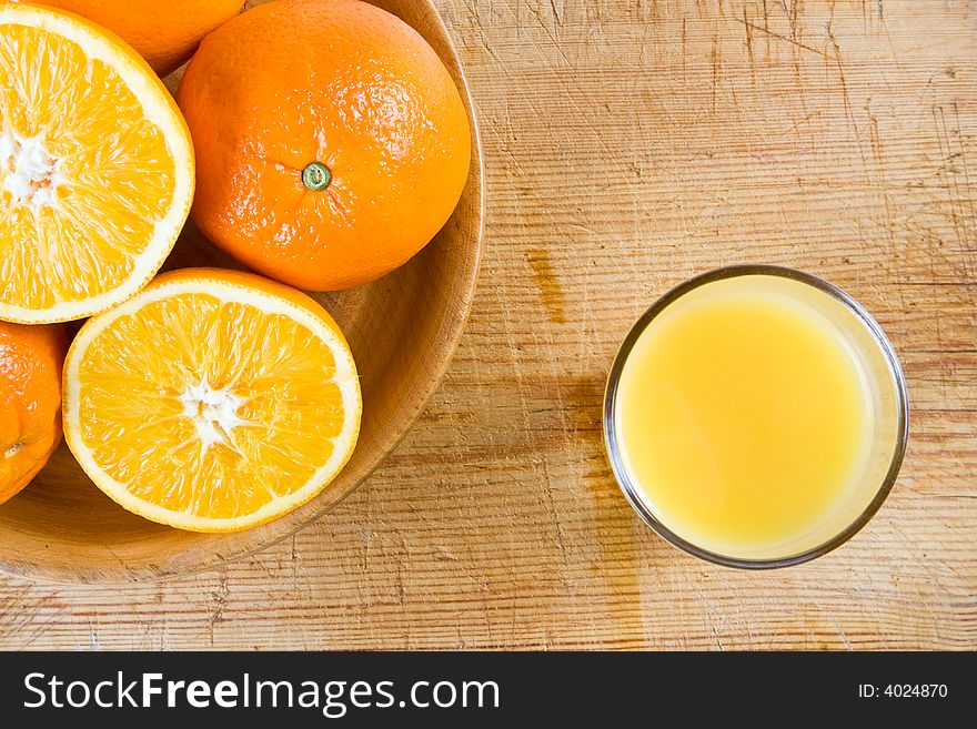 Two halves of orange in a wooden bowl with uncut oranges and a glass of orange juice. Two halves of orange in a wooden bowl with uncut oranges and a glass of orange juice