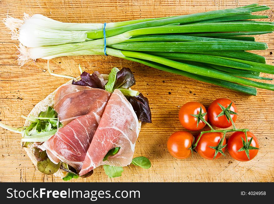 Bagel sandwich with spring onions and tomatoes on a wooden board