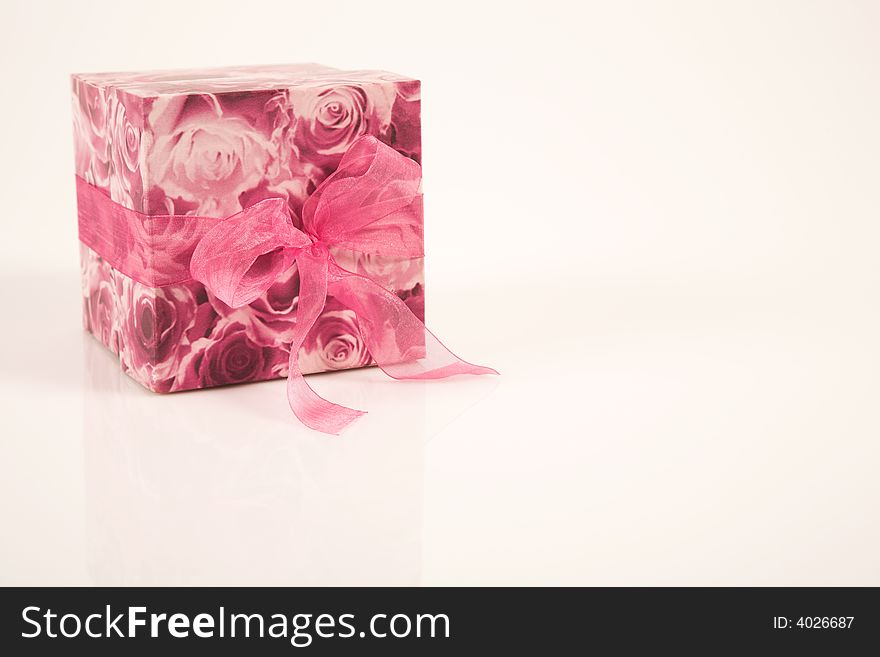 A floral patterned box lying on the side,  on a pastel pink background. It has a cerise pink ribbon around it. A floral patterned box lying on the side,  on a pastel pink background. It has a cerise pink ribbon around it.