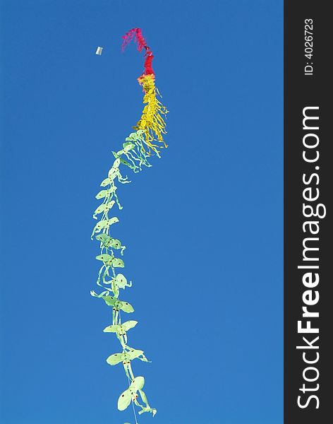 String of kites in the colours green, yellow and red on a blue sky background. Shallow depth of field with the nearest kites in focus.