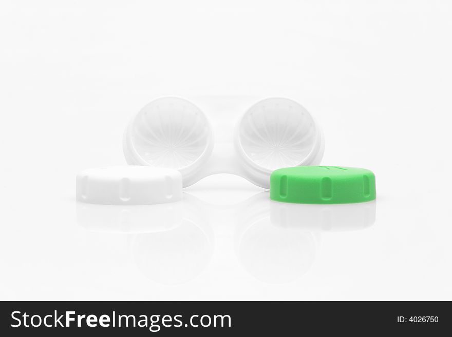 A white contact lens case on a white surface. One of the compartment lids is lime green. The lids are placed in front of the holder. A white contact lens case on a white surface. One of the compartment lids is lime green. The lids are placed in front of the holder