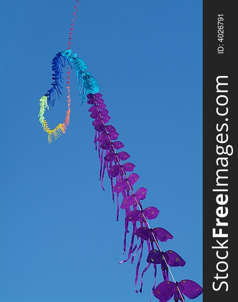 String of kites in assorted colours on a blue sky background. Shallow depth of field with the nearest kites in focus.