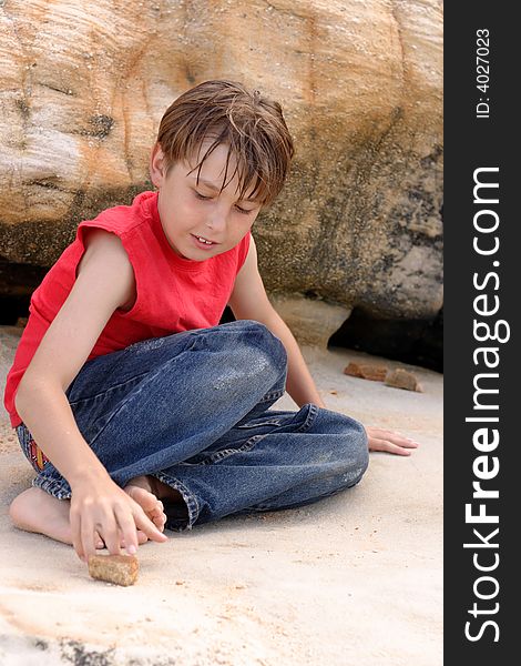 A casually dressed boy amuses himself playing with stones among sandstone rocks outdoors. A casually dressed boy amuses himself playing with stones among sandstone rocks outdoors