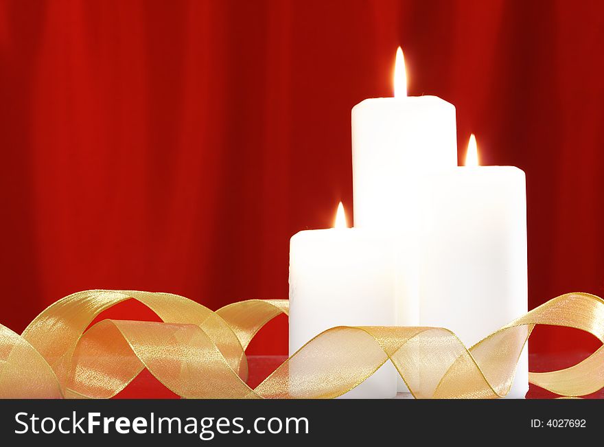 Candles and golden ribbon in front of red satin background. Candles and golden ribbon in front of red satin background